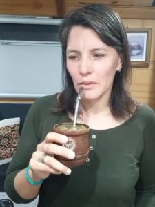 Mujer tomando mate en el interior de un motorhome, con mirada reflexiva y gesto contenido. Lleva una remera verde y sostiene el mate cerca de su boca. La expresión transmite introspección, cansancio y decisión, en un intento por pensar quién quiere ser.